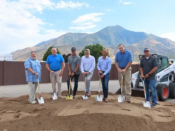 A group of men are standing in the dirt with shovels in front of a mountain.