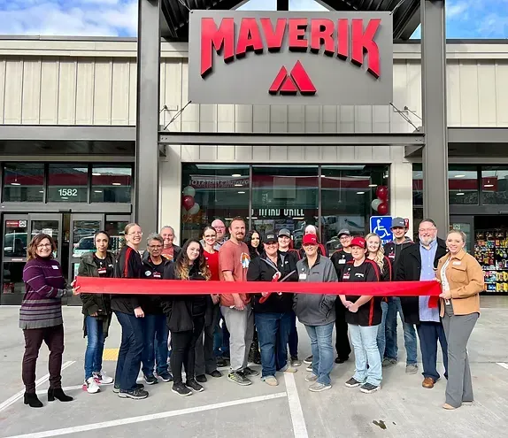 A group of people are standing in front of a maverick store holding a red ribbon.