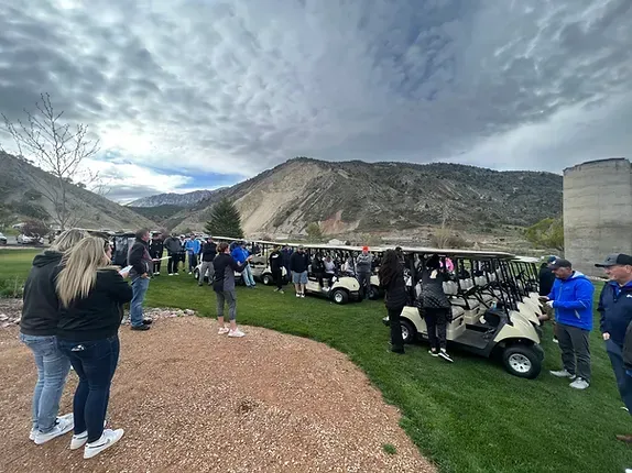 A group of people are standing around golf carts on a golf course.
