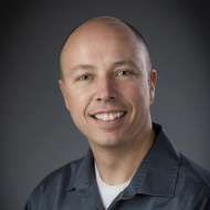 A man in a suit and plaid shirt is smiling for the camera.