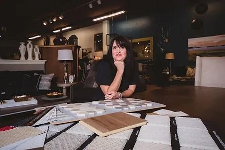 A woman is sitting at a table in a living room surrounded by furniture.