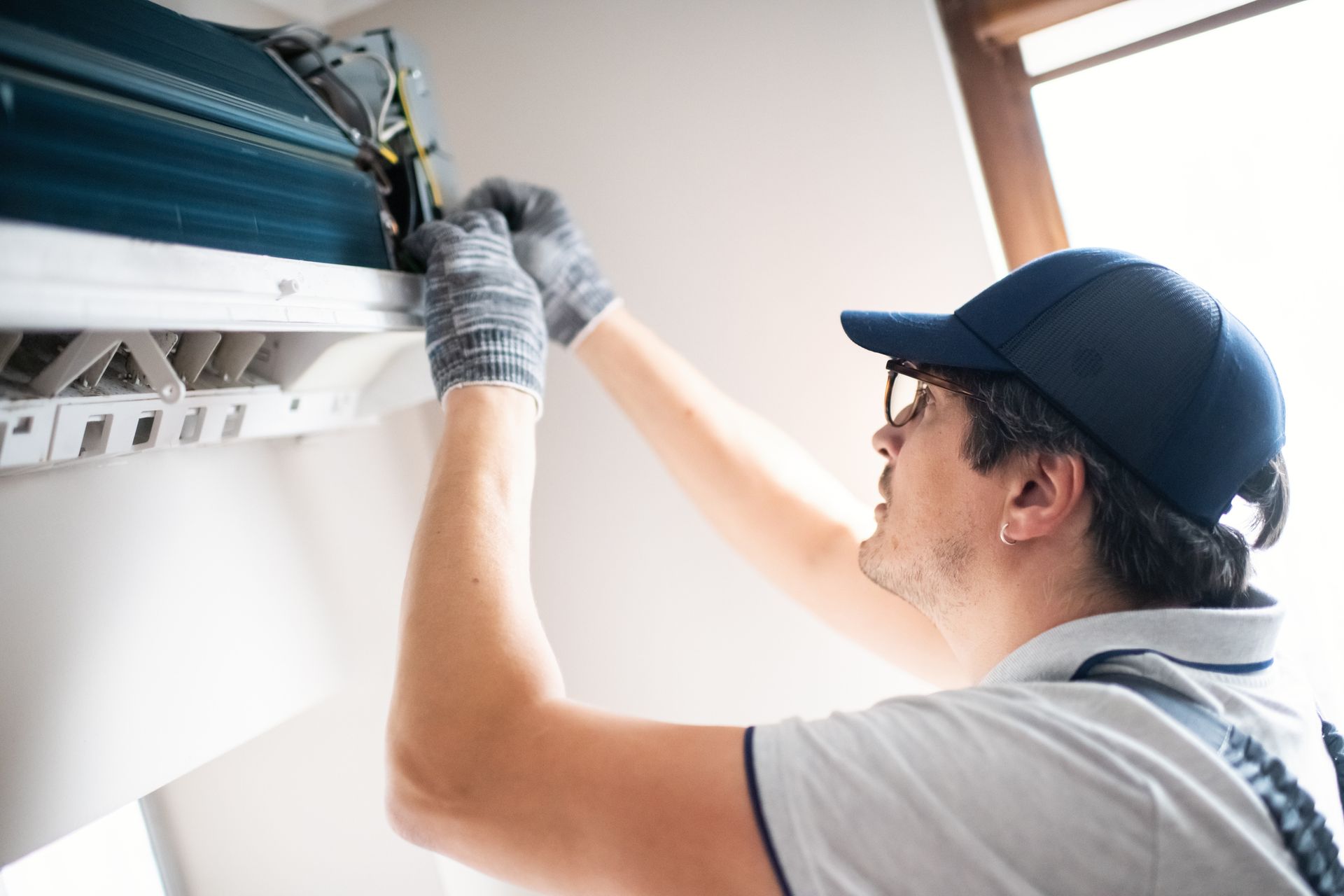 Male HVAC technician repairs an AC unit inside a room.