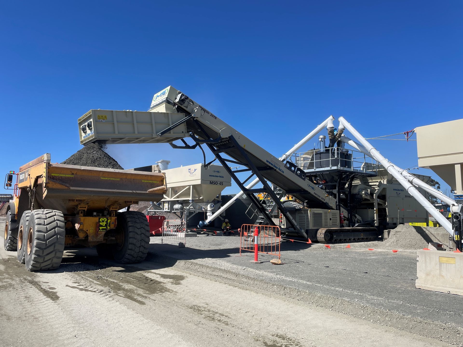 A dump truck is being loaded with gravel by a conveyor belt