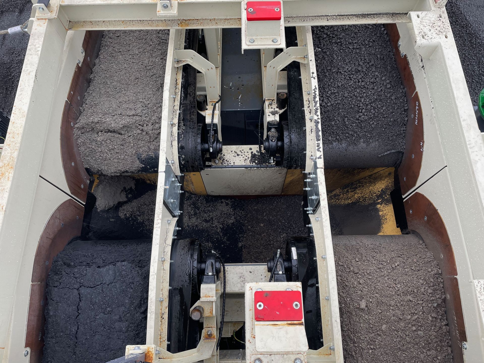 Top-down view of an asphalt paving machine, filled with black asphalt, and working on a road.