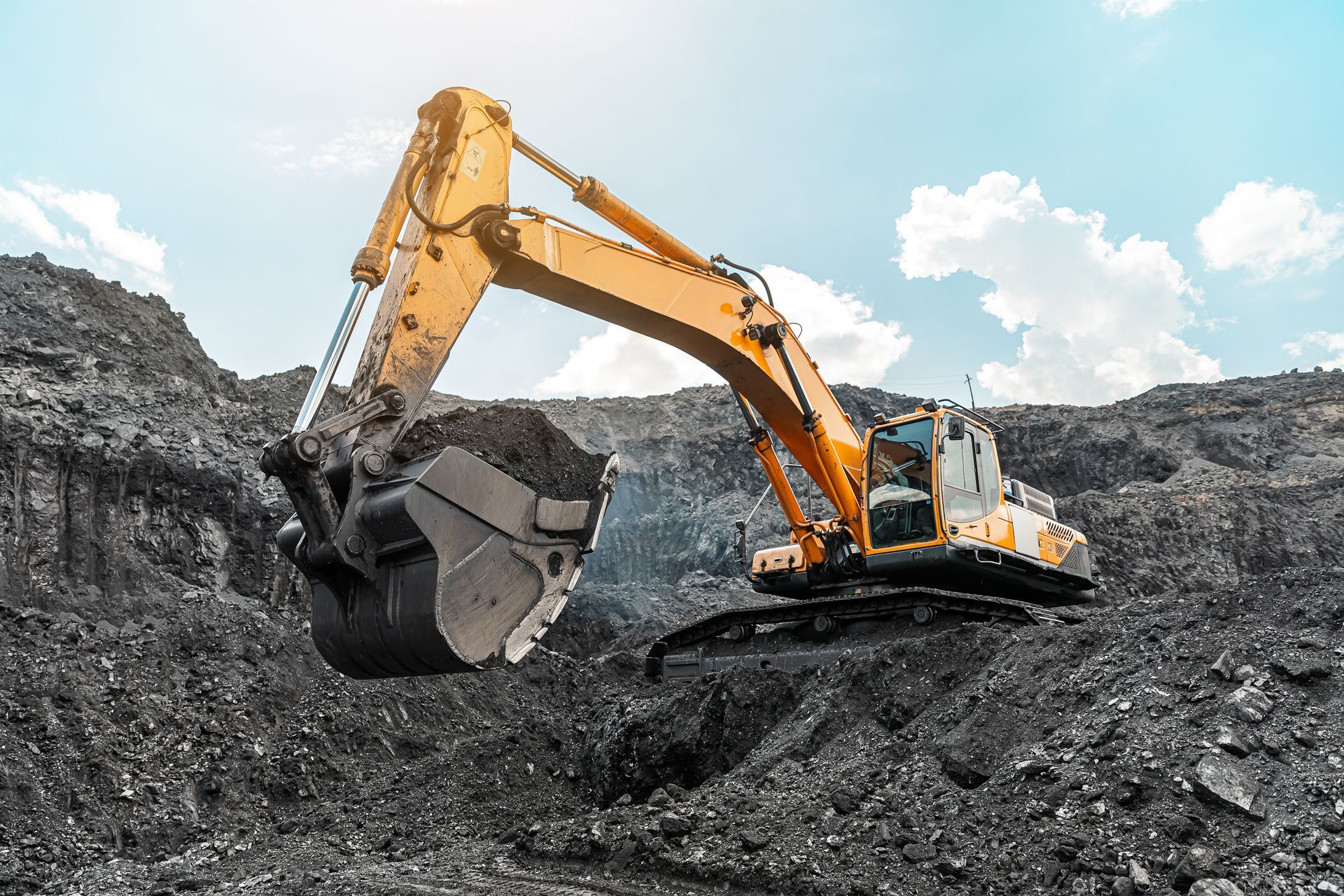 A big yellow quarry mining truck is at the work site, loading coal into the body of the truck.