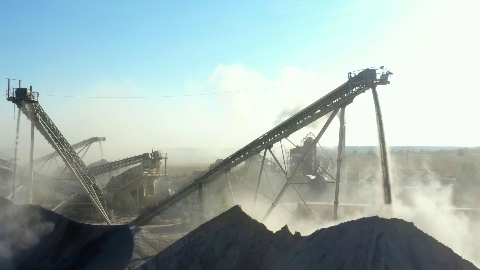 An industrial quarry with conveyors and machinery in a dusty setting. An industrial quarry with conveyors and machinery in a dusty setting.