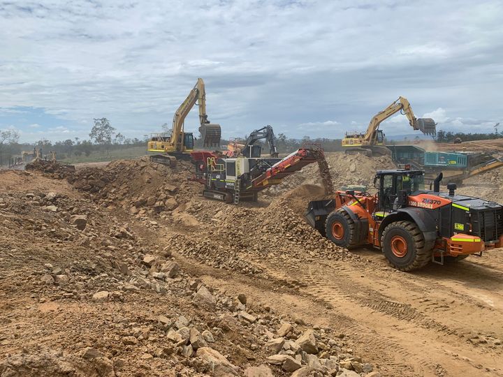 A group of construction vehicles are working on a dirt road.