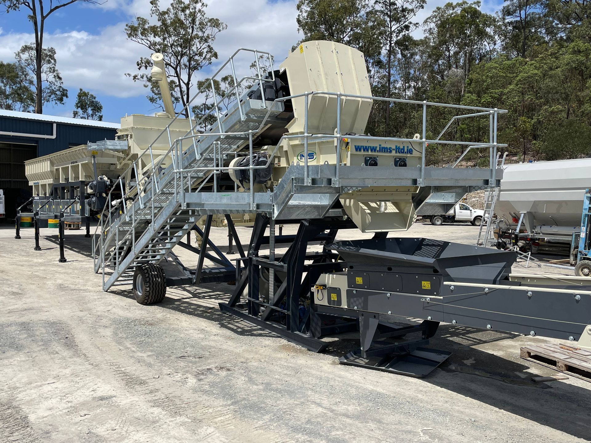 Mobile industrial machine, beige and gray, on wheels, outdoors, likely for material processing, with stairs and platforms.