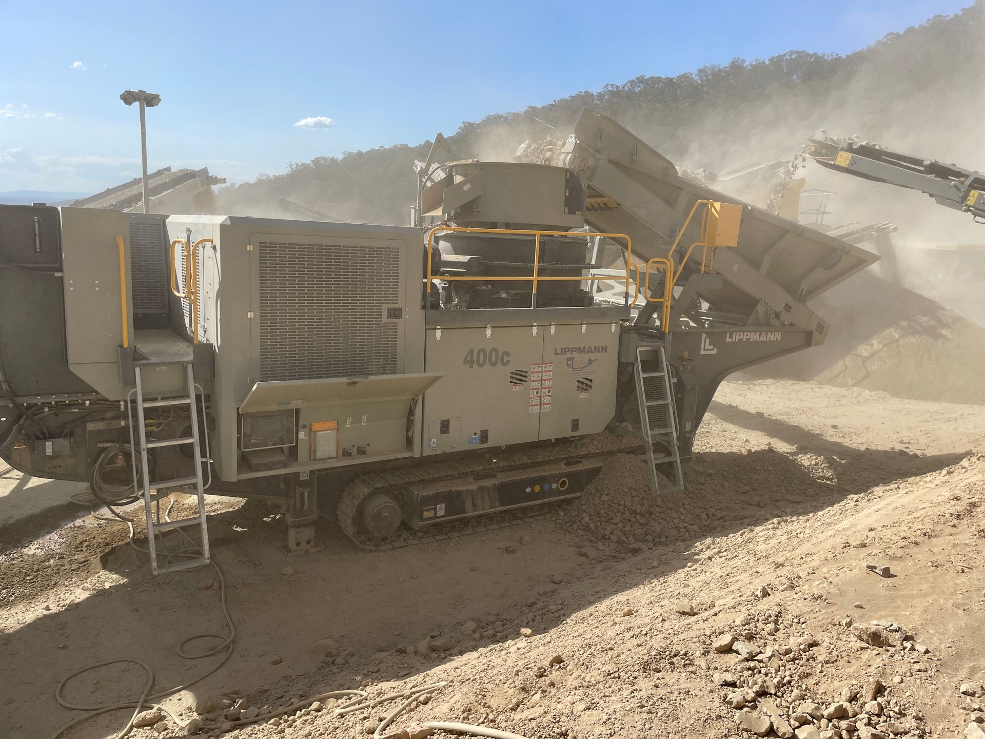 A large, mobile rock crusher in operation at a quarry, with a dusty environment and conveyor belts.