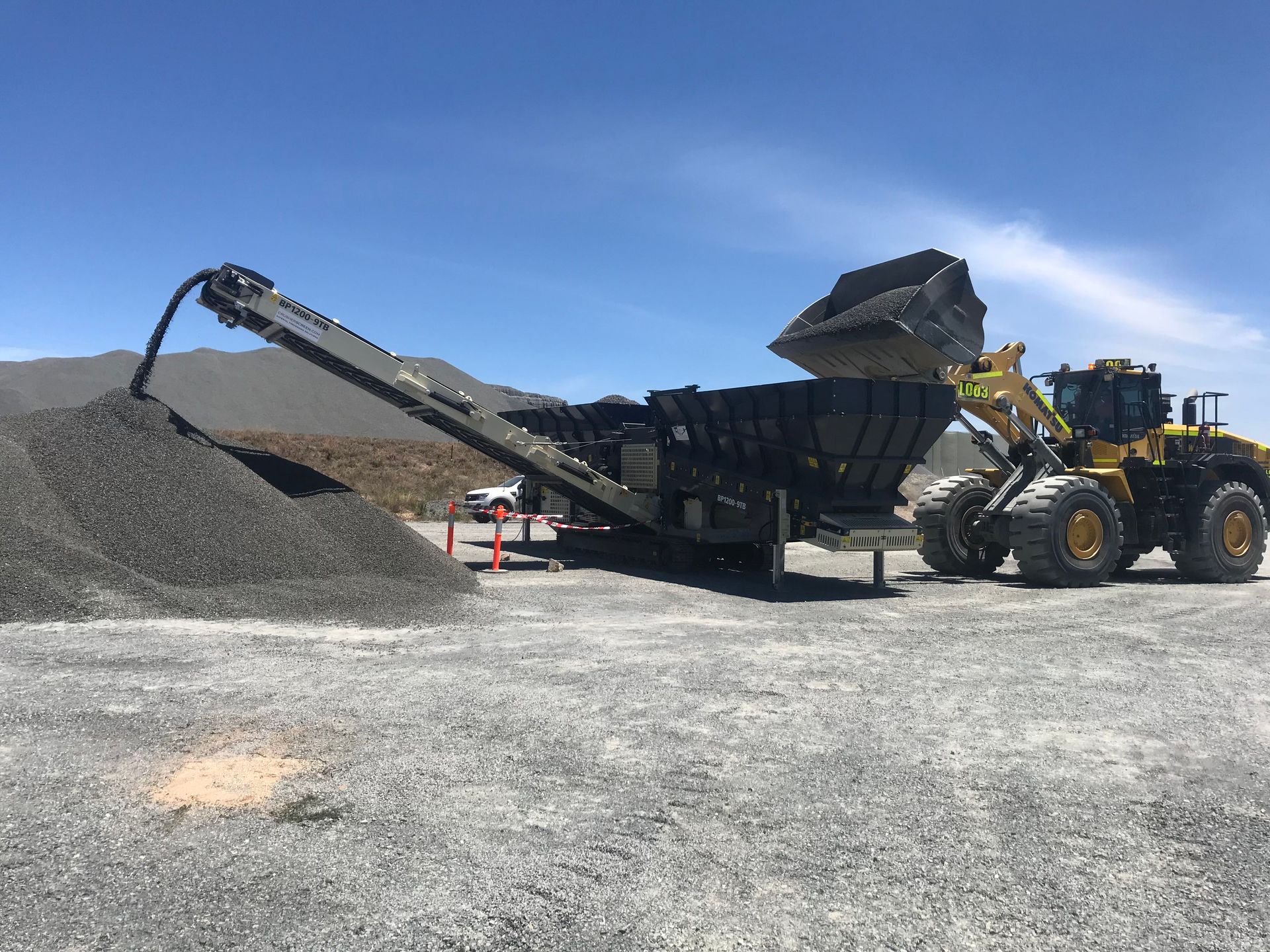 A bulldozer is loading gravel into a conveyor belt.