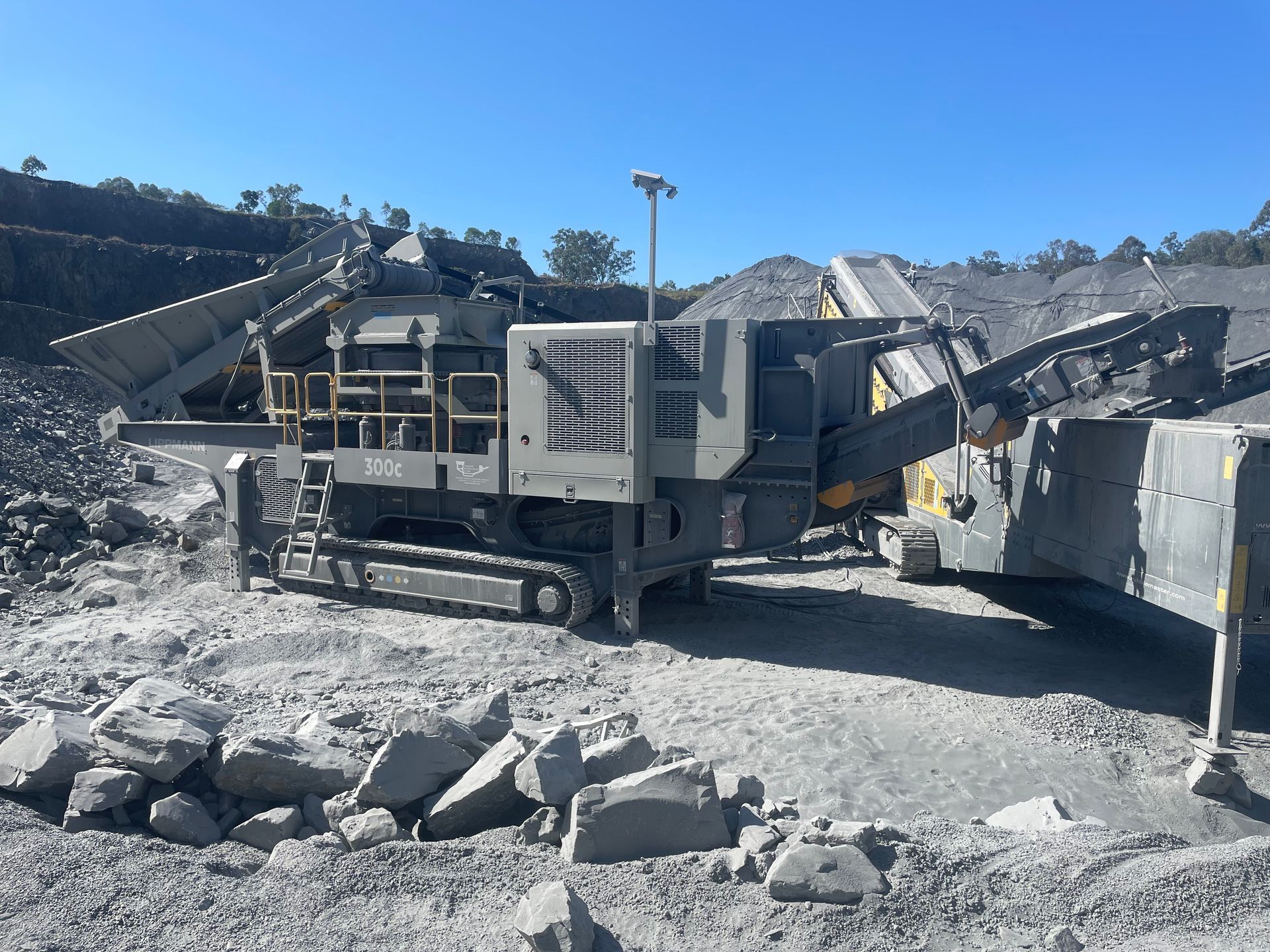 Mobile rock crusher on a rocky site, processing stones. A conveyor belt is extending out. The day is sunny.