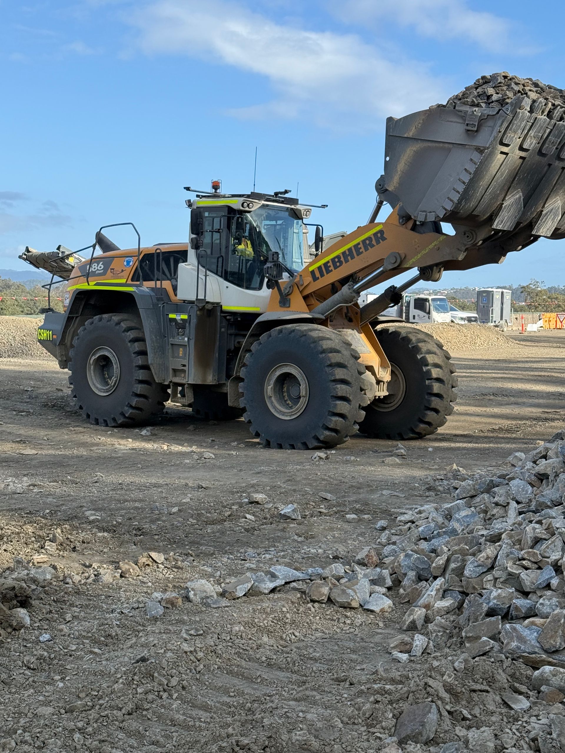 Yellow Liebherr wheel loader scoops up rubble on a construction site under a blue sky.