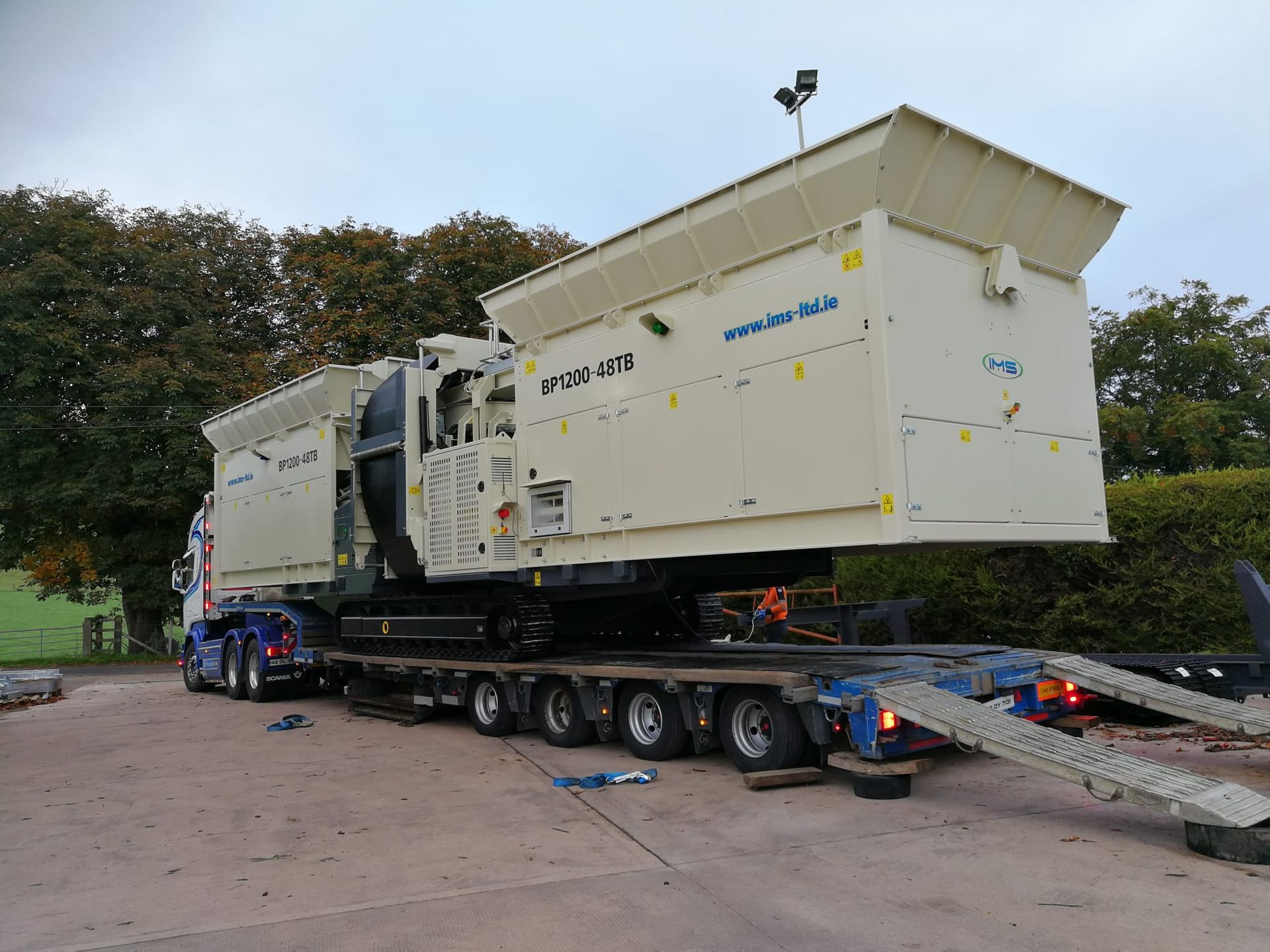 Large industrial machine, beige and boxy, loaded on a low-bed trailer. It's on a truck in an outdoor setting, presumably for transport.