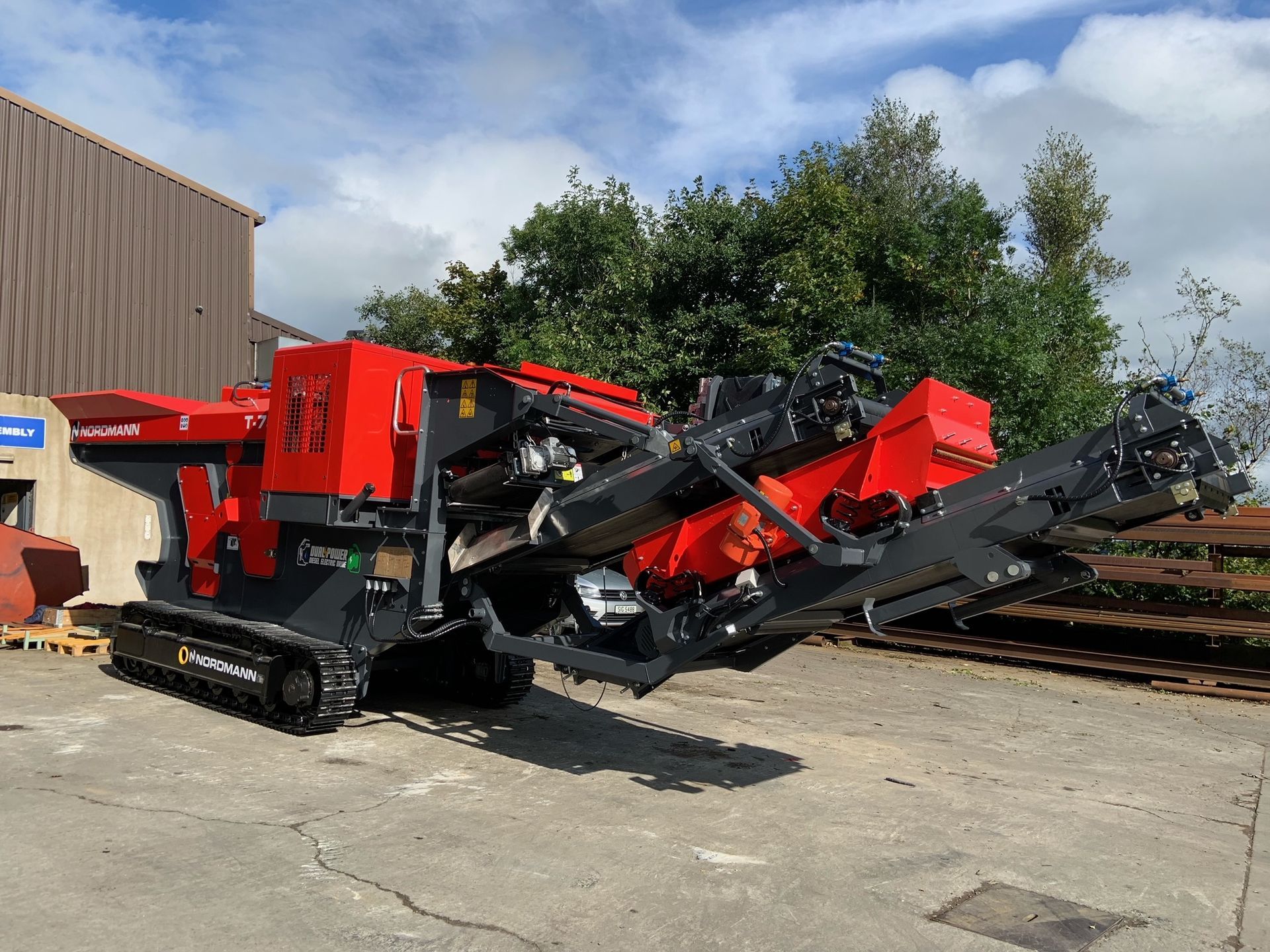 Red and black industrial crusher machine on tracks outside a building, used for processing materials.