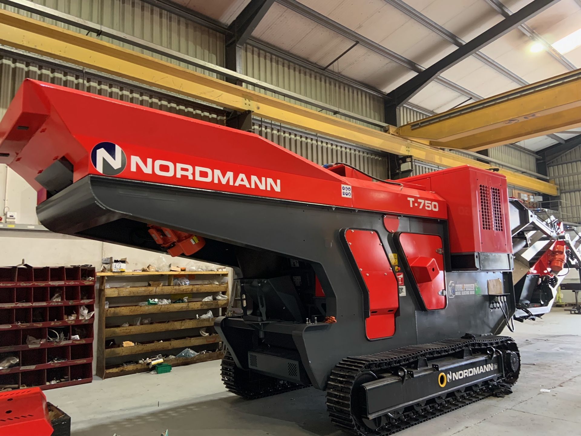 A red and black Nordmann T-2900 tracked mobile shredder in a workshop. The machine has a large hopper, tracks, and a cutting mechanism.