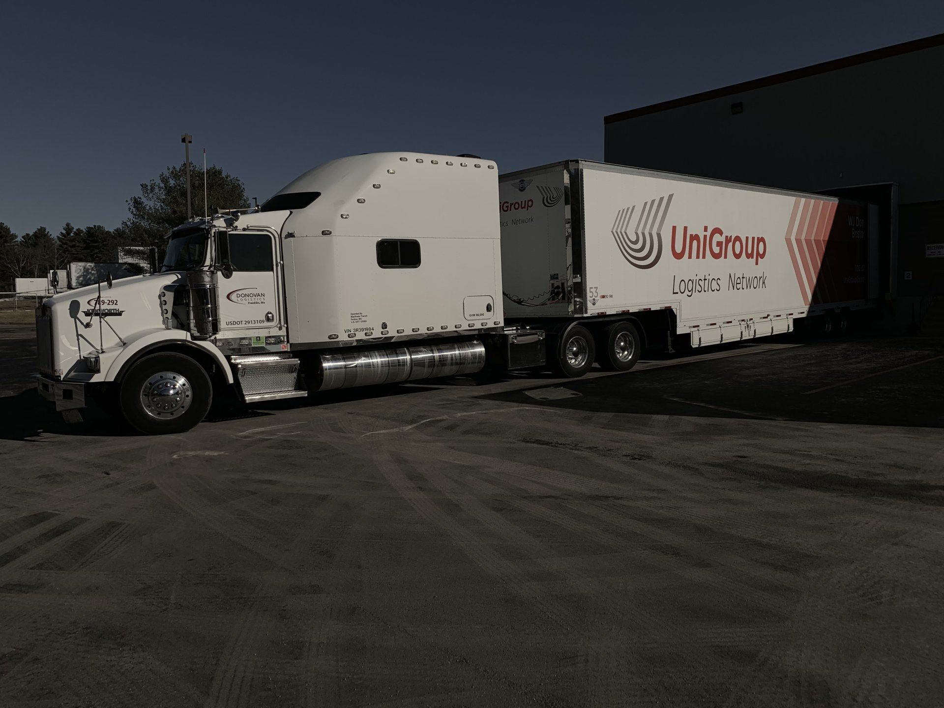 White semi-truck parked beside a UniGroup moving trailer on a sunny lot