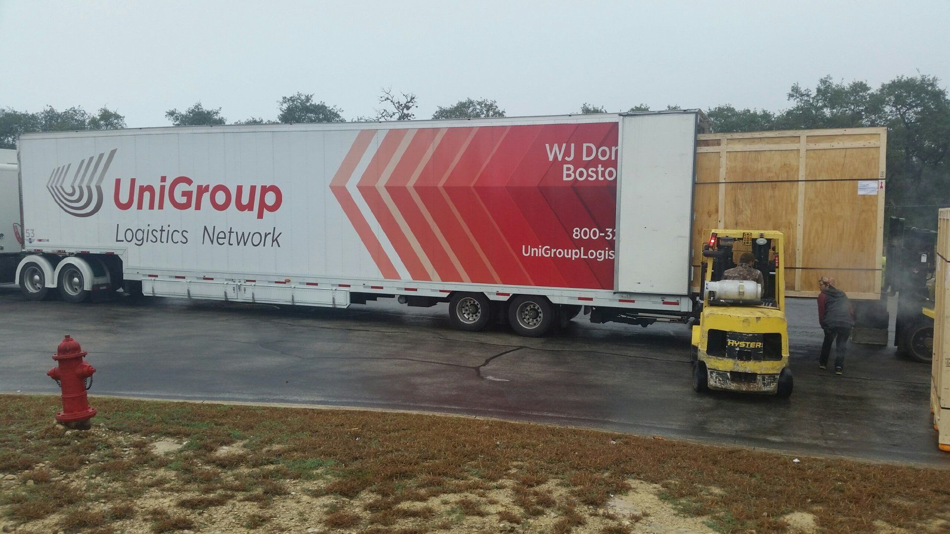 White UniGroup moving truck with forklift loading at a warehouse on a rainy lot