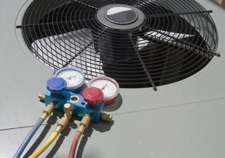 HVAC service manifold gauges with blue, yellow, and red hoses connected to a residential outdoor air conditioner unit.