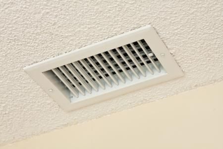 A white rectangular ceiling air vent with horizontal slats, mounted on a textured white ceiling.
