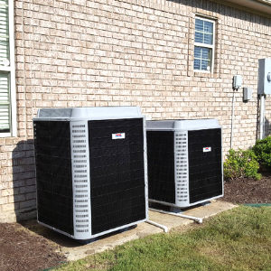 Two HVAC outdoor condenser units sitting on concrete pads against a brick exterior wall of a house.