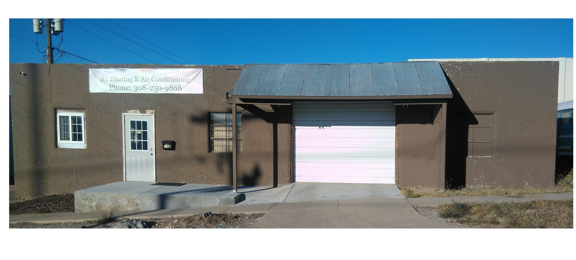 A brown commercial building with a white door, a large garage-style door, and a sign above the door against a blue sky.