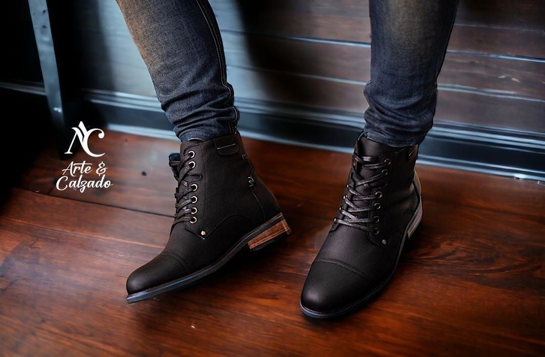 Botas marrones de cuero con cordones, combinadas con vaqueros azules remangados sobre un fondo marrón liso.