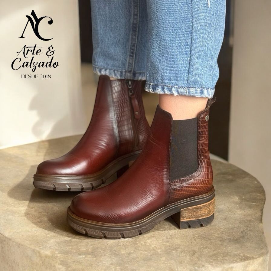 Un par de botines Chelsea de piel color burdeos con tacones con relieve de cocodrilo, combinados con vaqueros remangado