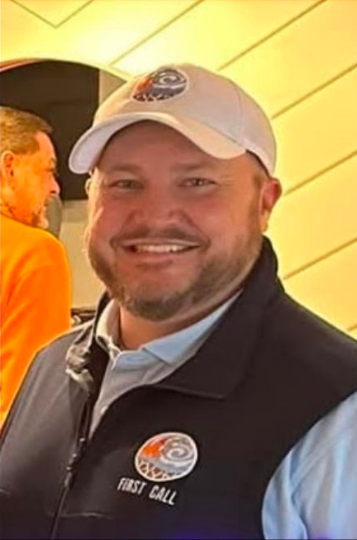 Man wearing white cap and vest smiling. 