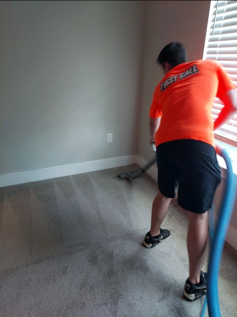 Person in orange shirt cleaning carpet with a vacuum in a room.