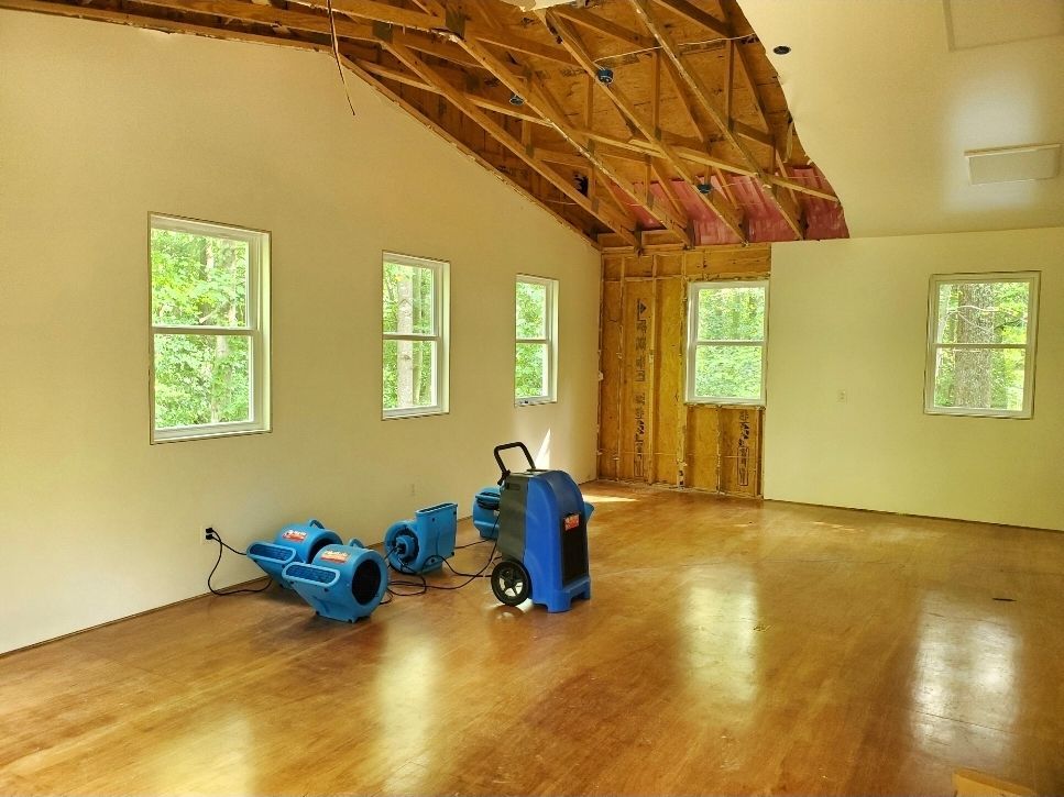 An empty room with wood floors, several windows, and three blue air movers.