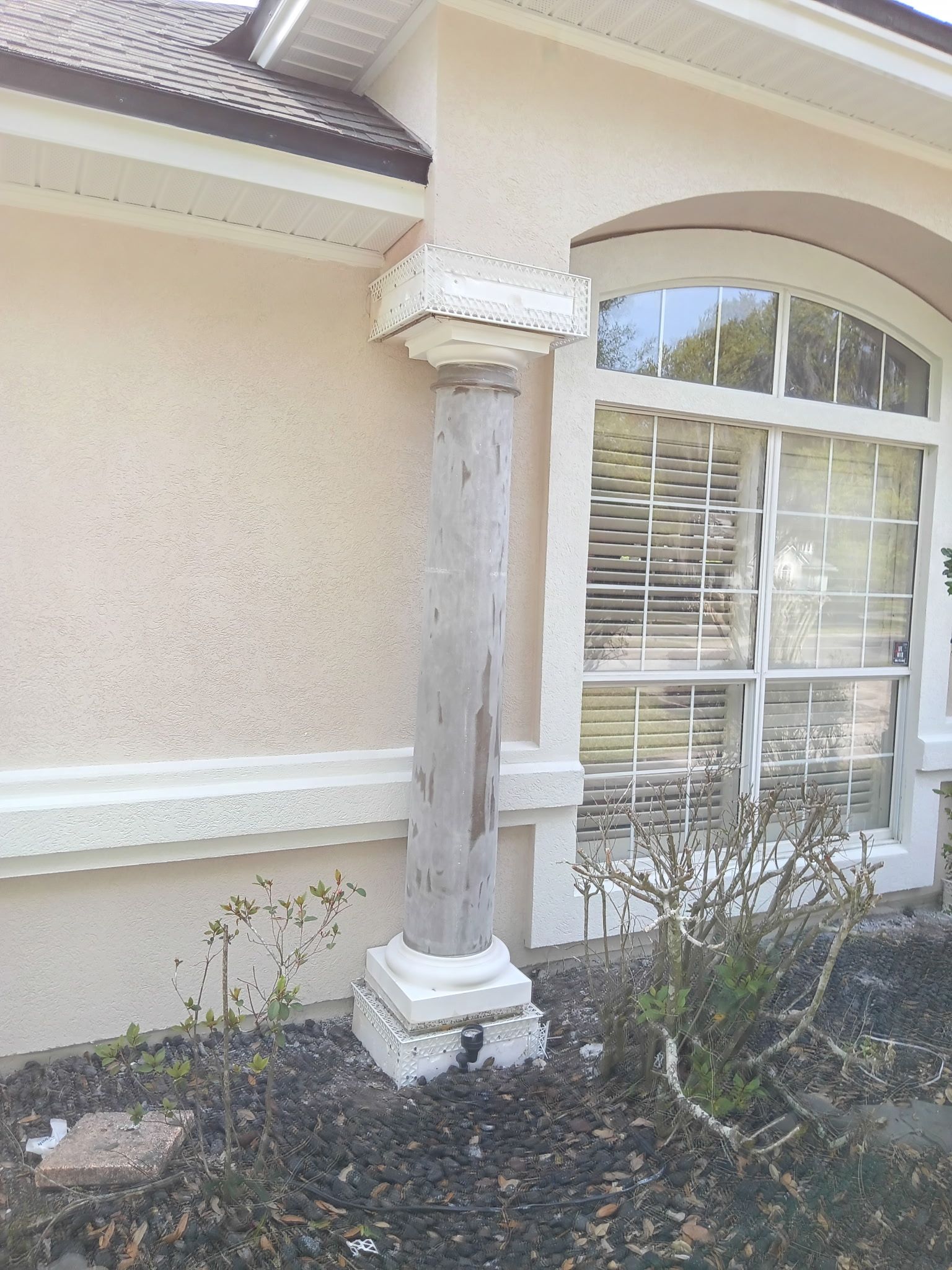 A weathered, white stucco column outside a building with a window.