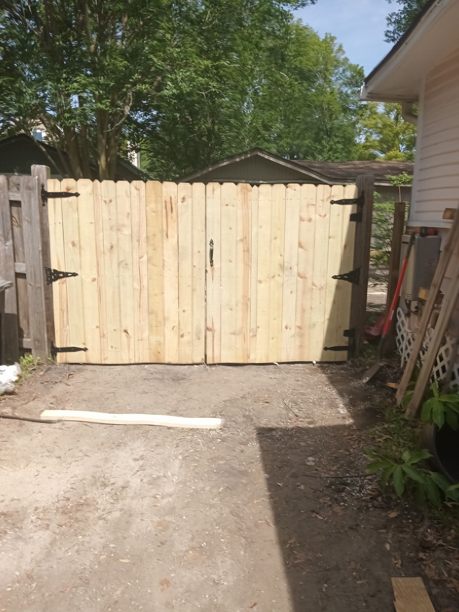Wooden gate in a backyard, secured by black hinges and a latch, between wooden and vinyl fences.