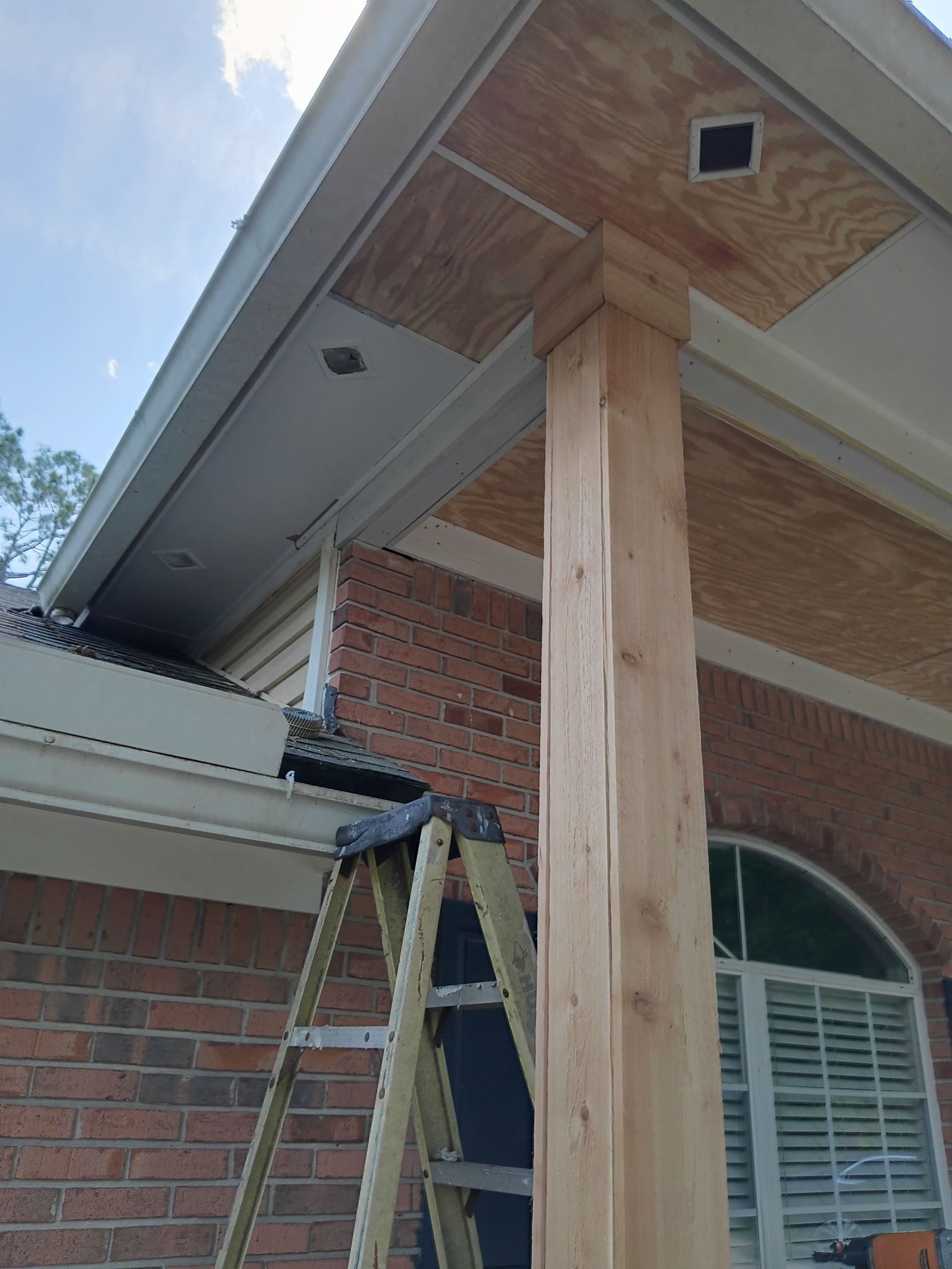Ladder propped against brick wall; wooden pillar and ceiling under a roof.