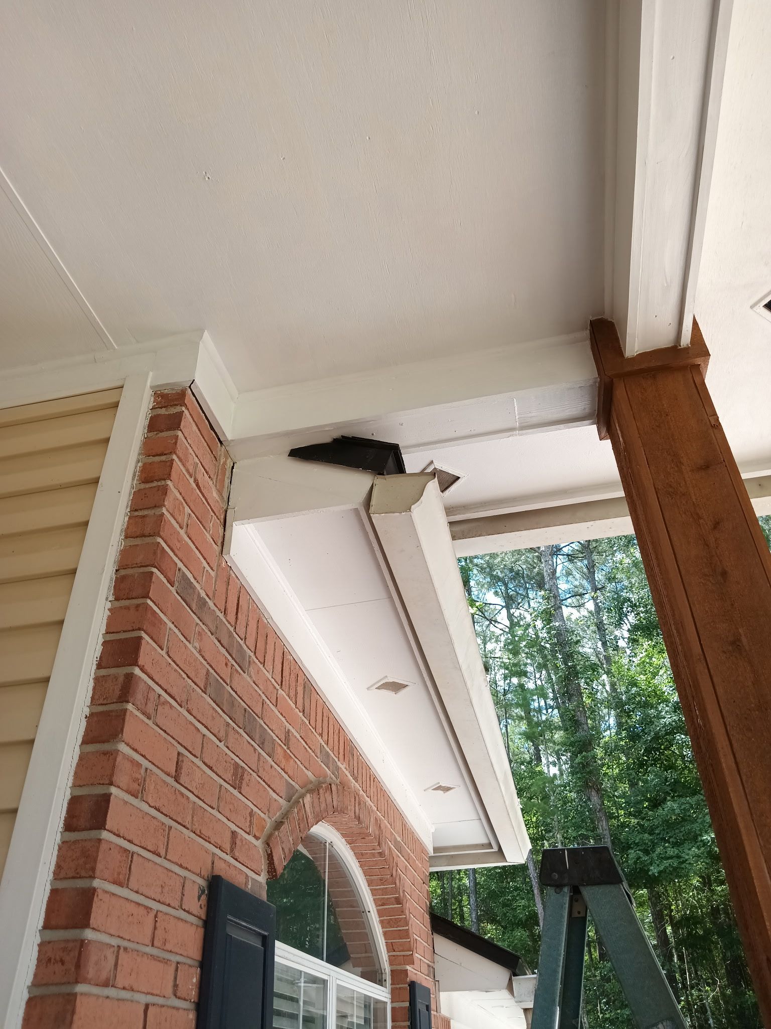 Brick and siding exterior with a dark object nestled under the porch roof.