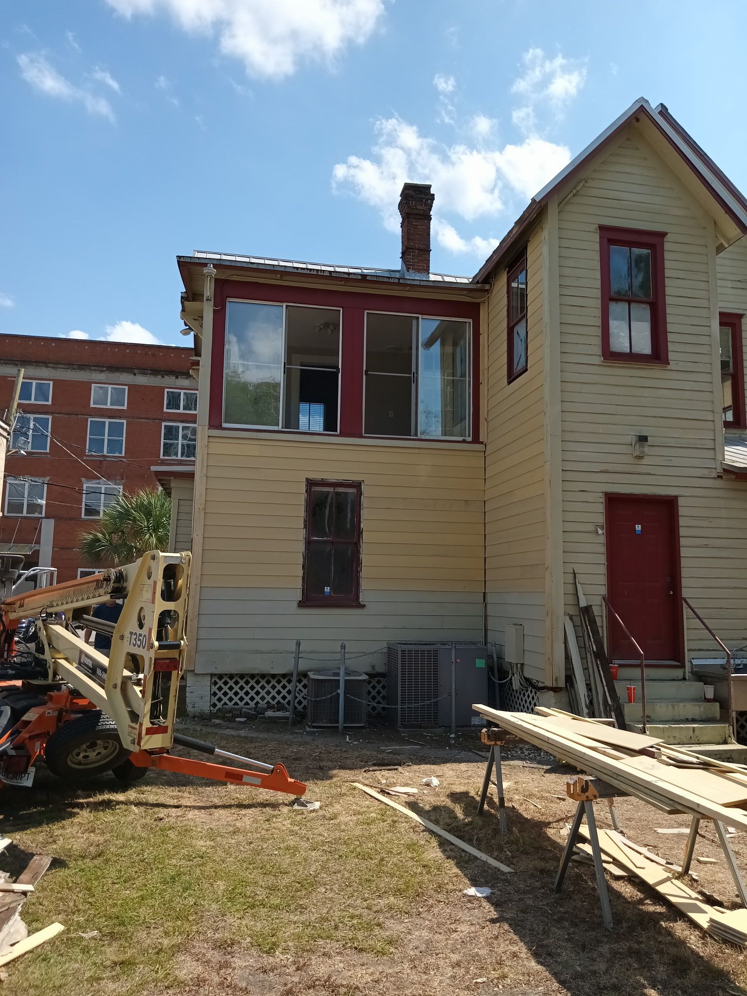 Back of a two-story yellow house with a red door and window trim. A sunroom is under construction.