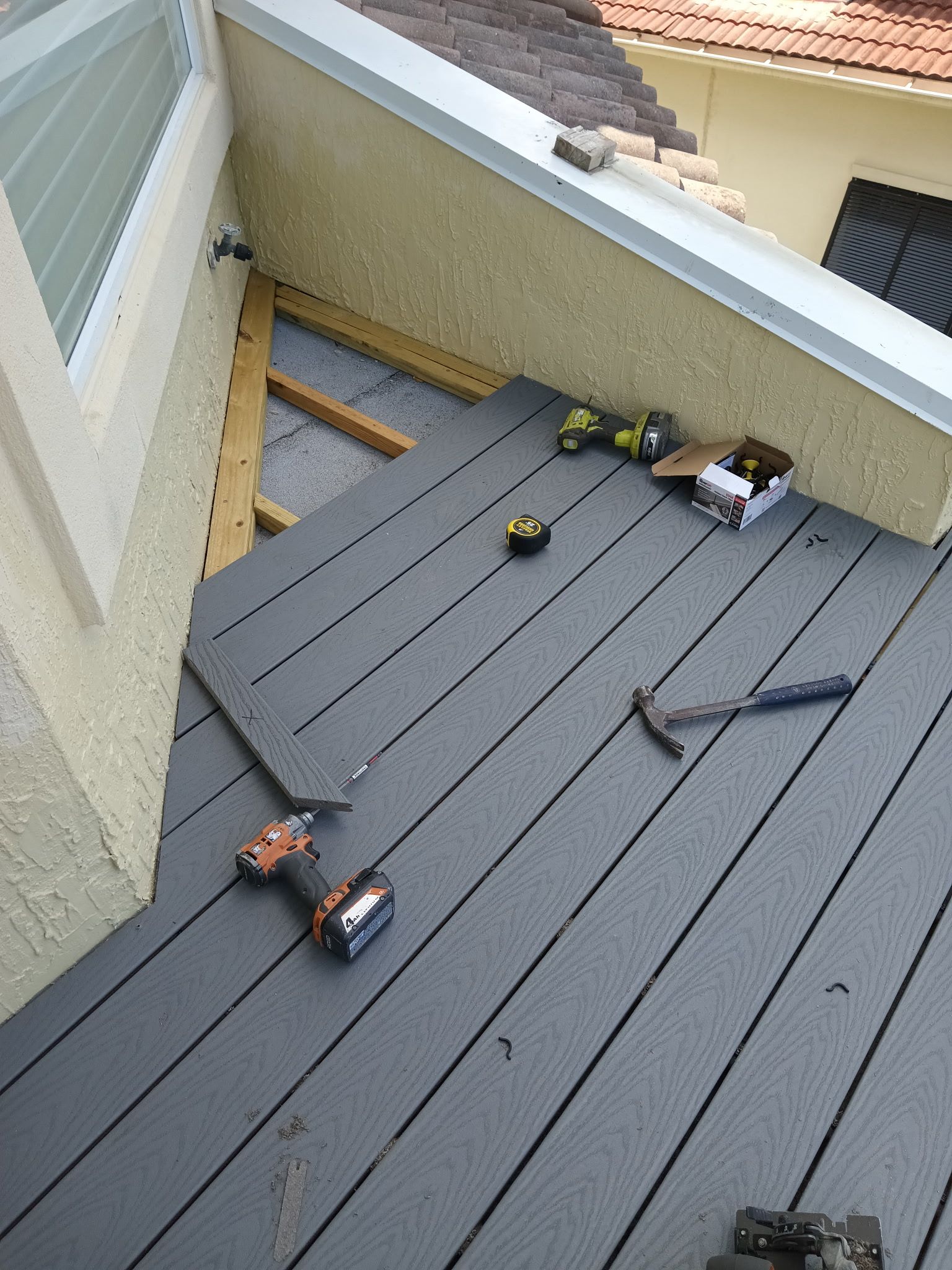 Gray composite decking being installed near a building with tools scattered nearby.