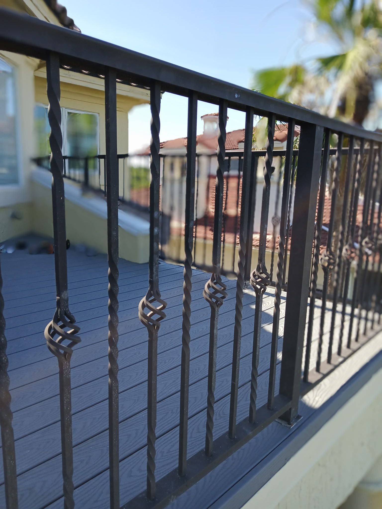 Black metal railing with decorative elements on a deck overlooking a residential area on a sunny day.