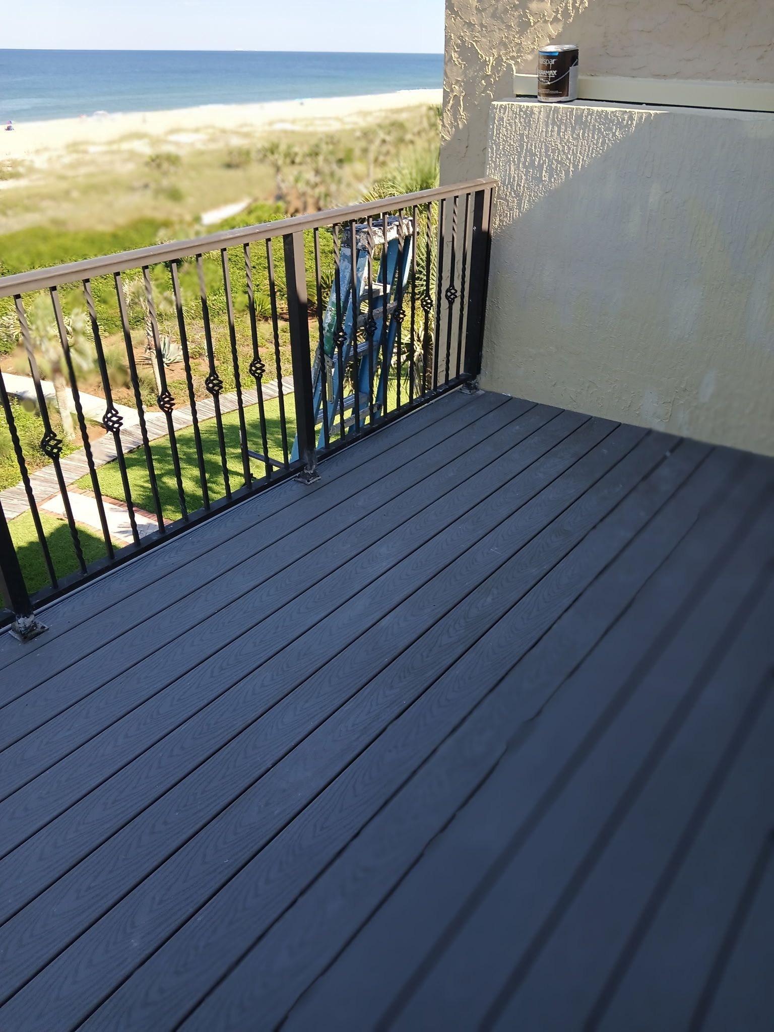 Deck overlooking beach and ocean; black railings, gray deck boards, sunny outdoor setting.