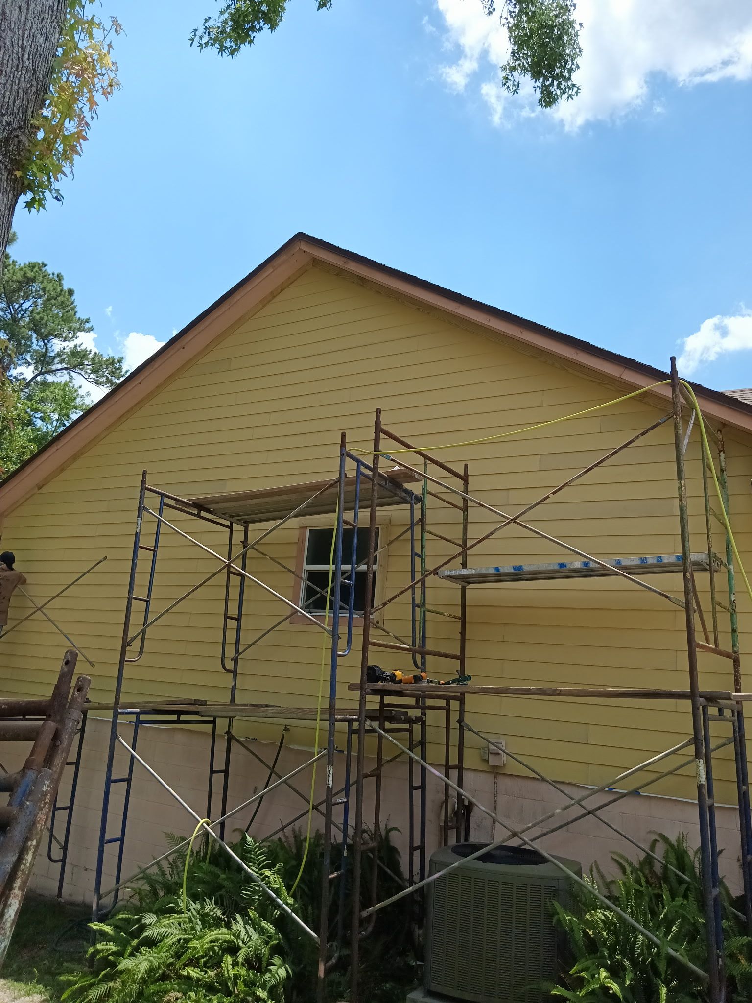 Scaffolding in front of a house. Yellow siding covers the side of the house. A window is in the center.