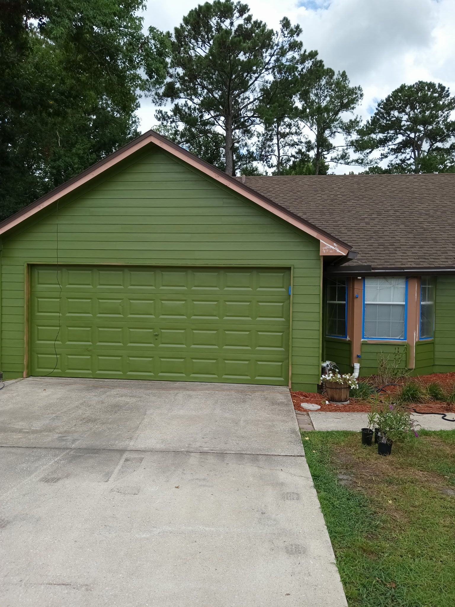 Green house with a garage, brown roof, and a concrete driveway.