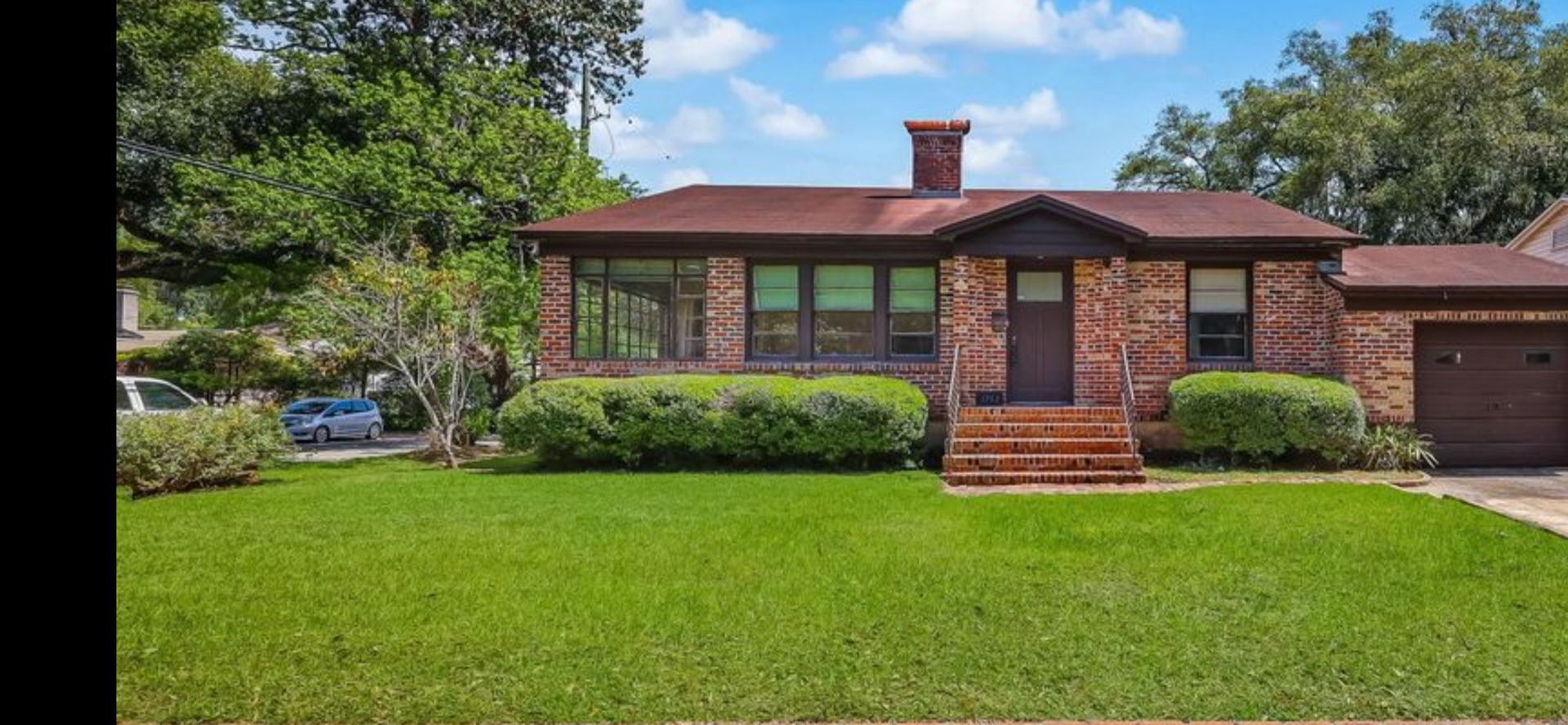 A brick bungalow with a brown roof, garage, and green lawn under a blue sky.