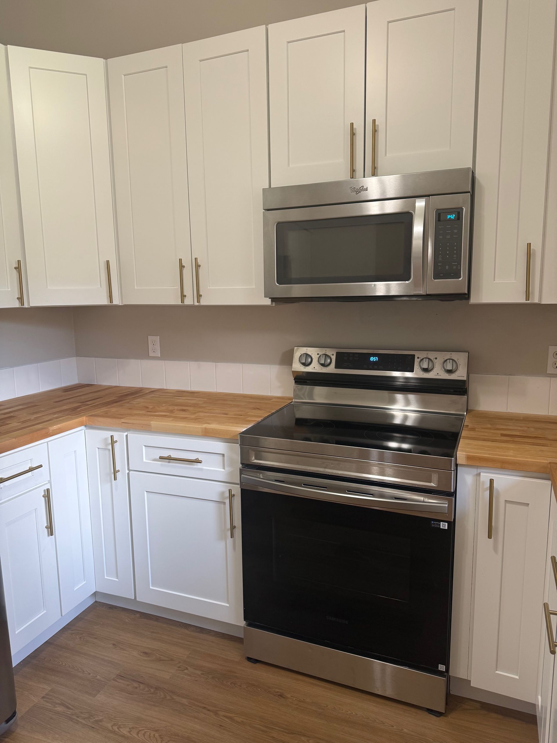 White kitchen cabinets with butcher block countertops and stainless steel appliances.