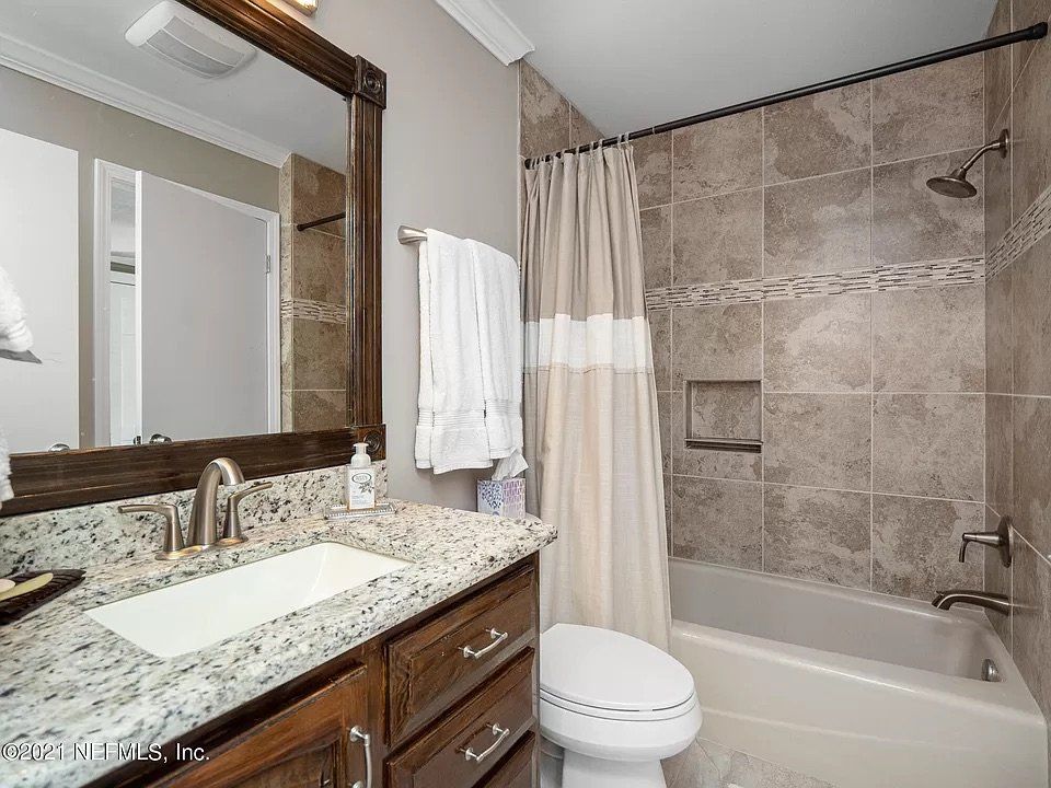 Bathroom with granite countertop, brown cabinetry, and tiled shower.