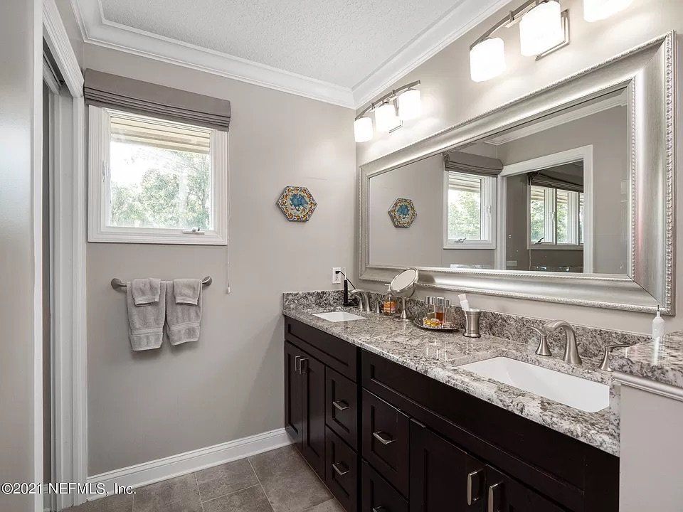 Bathroom with dark brown double vanity, gray walls, large mirror, and window.