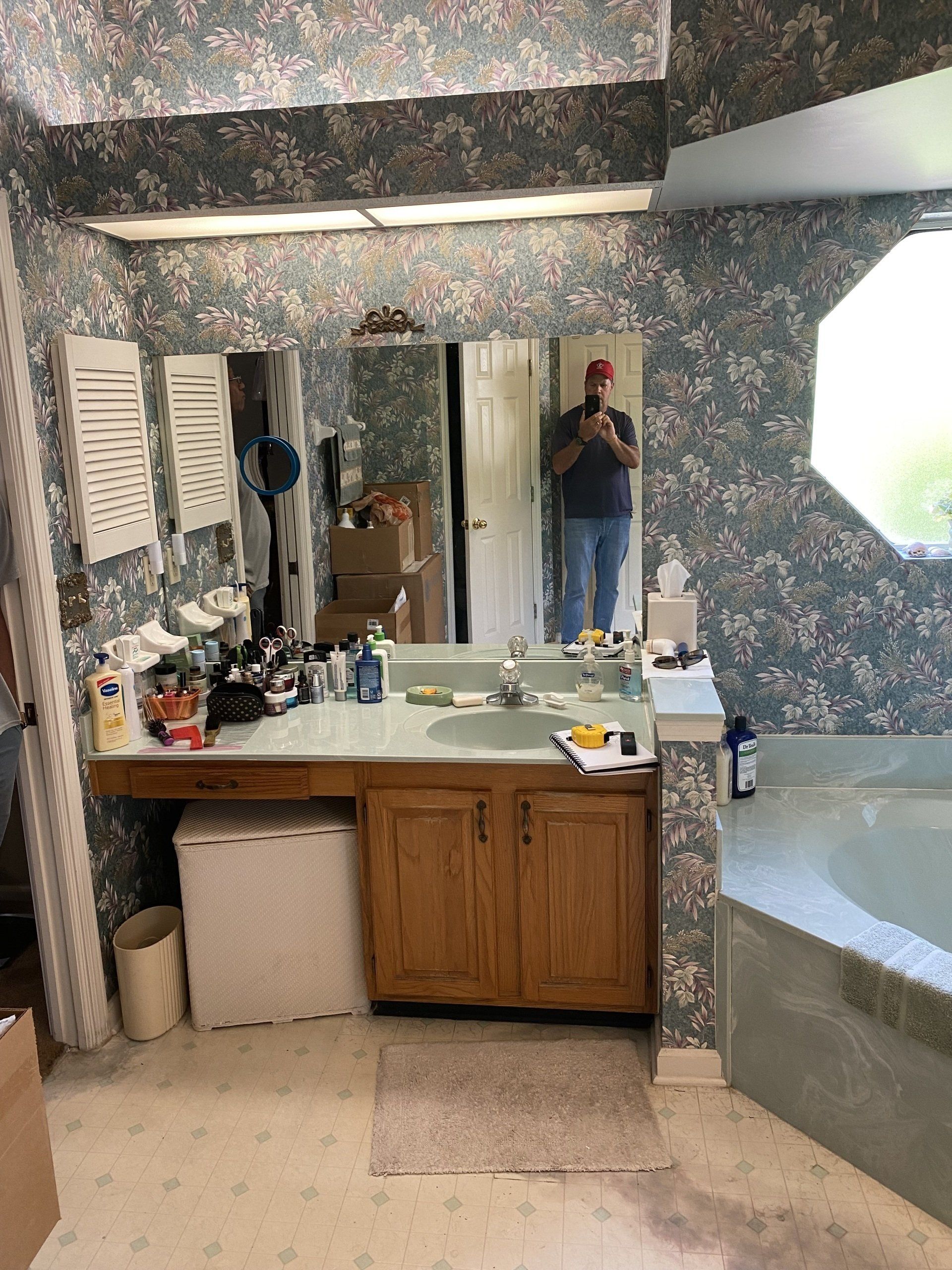 Bathroom with floral wallpaper, a person reflected in the mirror, and a built-in vanity with storage.
