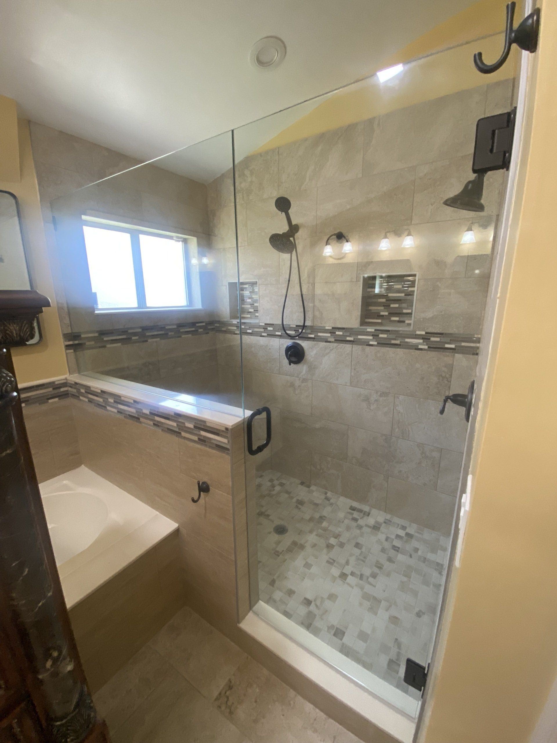 Bathroom with a tiled shower, glass door, and built-in bench. Beige and brown tones throughout.