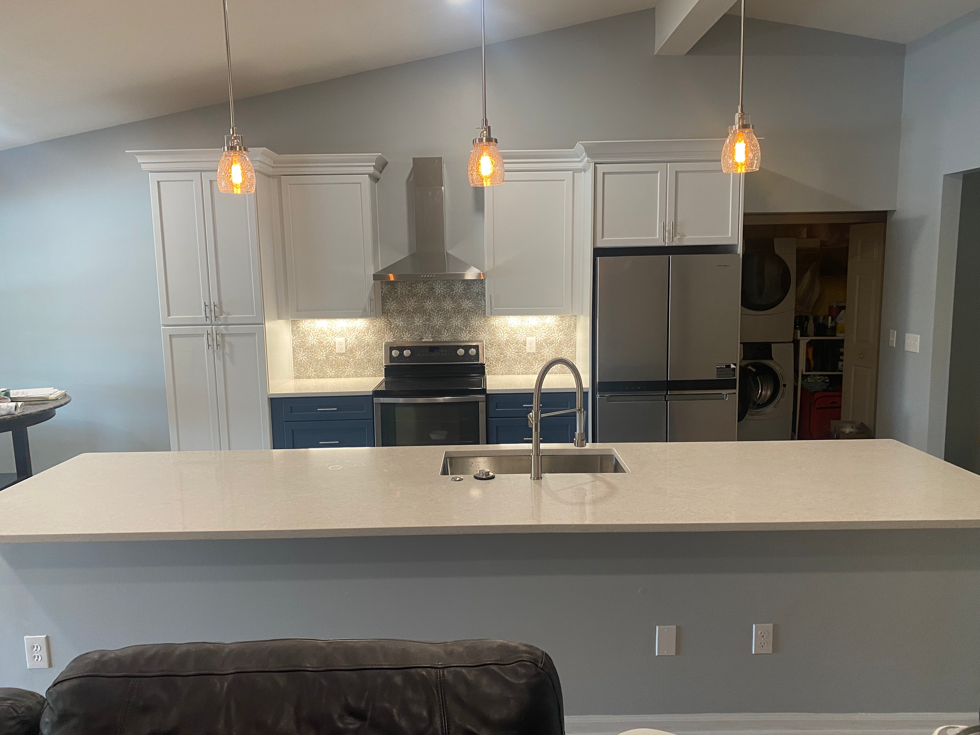 Modern kitchen with blue and white cabinets, stainless steel appliances, and a large island with pendant lights.