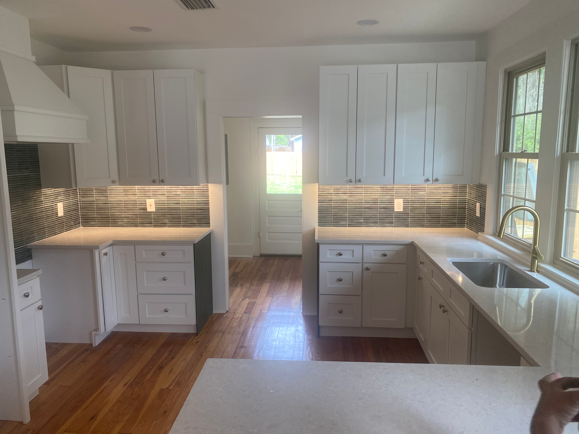 White kitchen with cabinets, countertops, and backsplash, along with hardwood flooring, and a window.