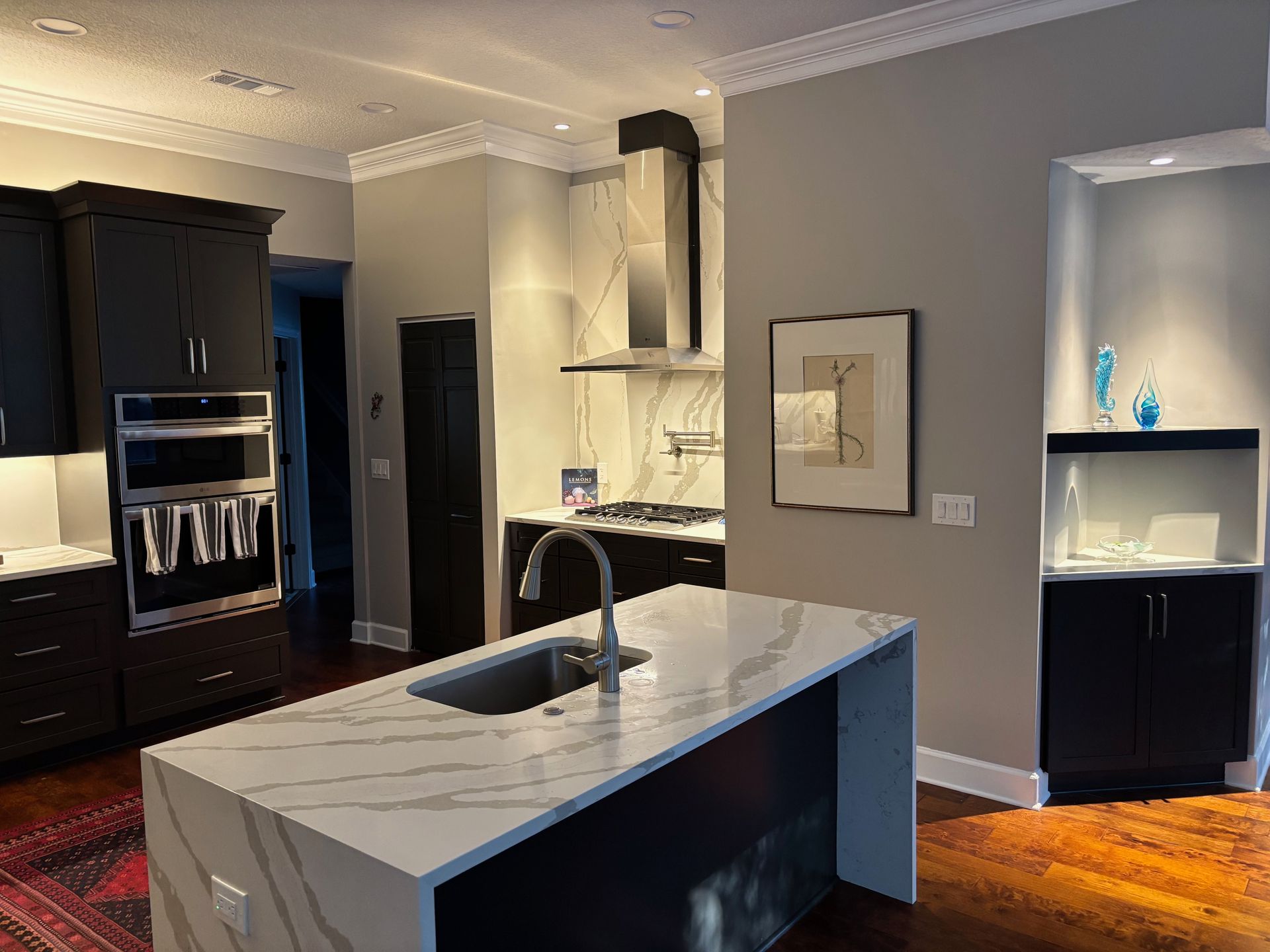Modern kitchen with black cabinets, white countertops, island sink, and stainless steel appliances.