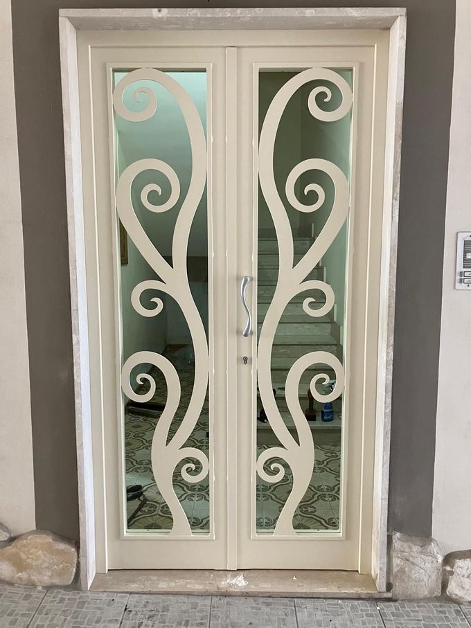 Doppie porte color avorio sporco con intricati motivi a spirale intagliati e pannelli in vetro, incastonate in una cornice di pietra.